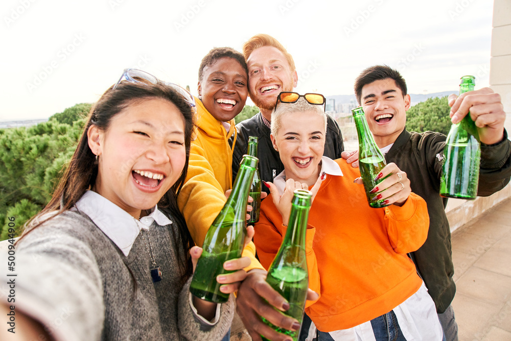 Smiling selfie of a happy group of multicultural friends holding beers looking at the camera. Portrait of cheerful multi-ethnic young people of diverse races having fun together.