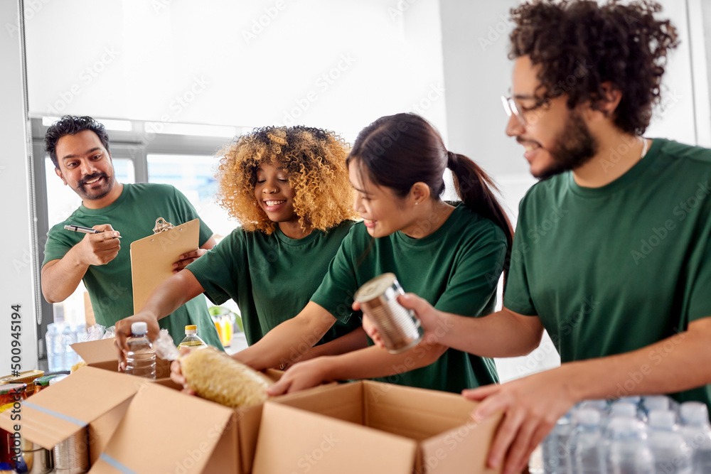 charity, donation and volunteering concept - international group of happy smiling volunteers packing food in boxes according to list on clipboard at distribution or refugee assistance center charity, donation and volunteering concept - international group of happy smiling volunteers packing food in boxes according to list on clipboard at distribution or refugee assistance center