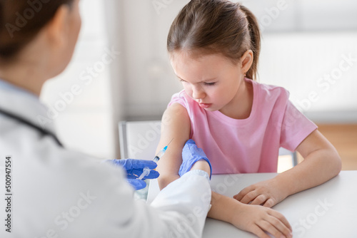 medicine, healthcare and vaccination concept - female doctor or pediatrician with syringe making vaccine injection to little girl patient at clinic