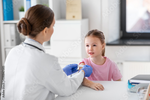 medicine, healthcare and vaccination concept - female doctor or pediatrician talking to little girl patient on medical exam at clinic