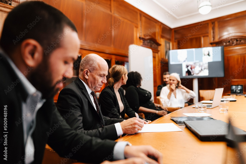 Male financial advisor signing agreement during meeting with colleagues in board room Male financial advisor signing agreement during meeting with colleagues in board room