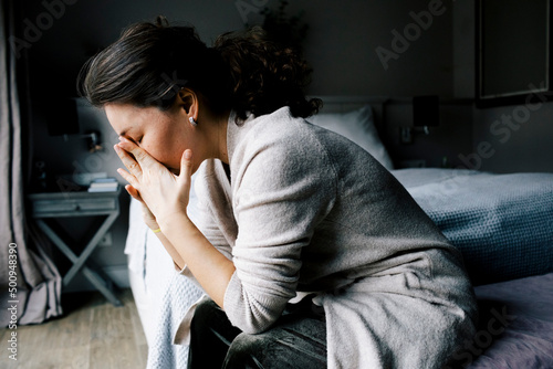 Side view of lonely anxious woman sitting by bed at home