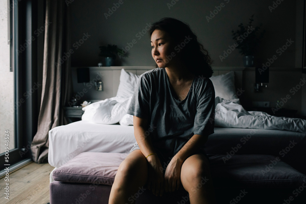 Mentally exhausted woman sitting on bed end bench in bedroom at home