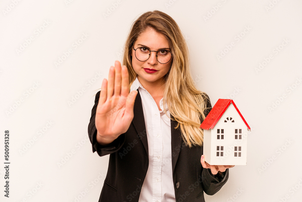 Young business caucasian woman holding a toy house isolated on white background standing with outstretched hand showing stop sign, preventing you. Young business caucasian woman holding a toy house isolated on white background standing with outstretched hand showing stop sign, preventing you.