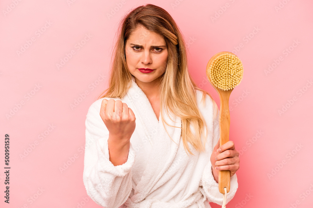Young caucasian woman holding back scratcher isolated on pink background showing fist to camera, aggressive facial expression. Young caucasian woman holding back scratcher isolated on pink background showing fist to camera, aggressive facial expression.