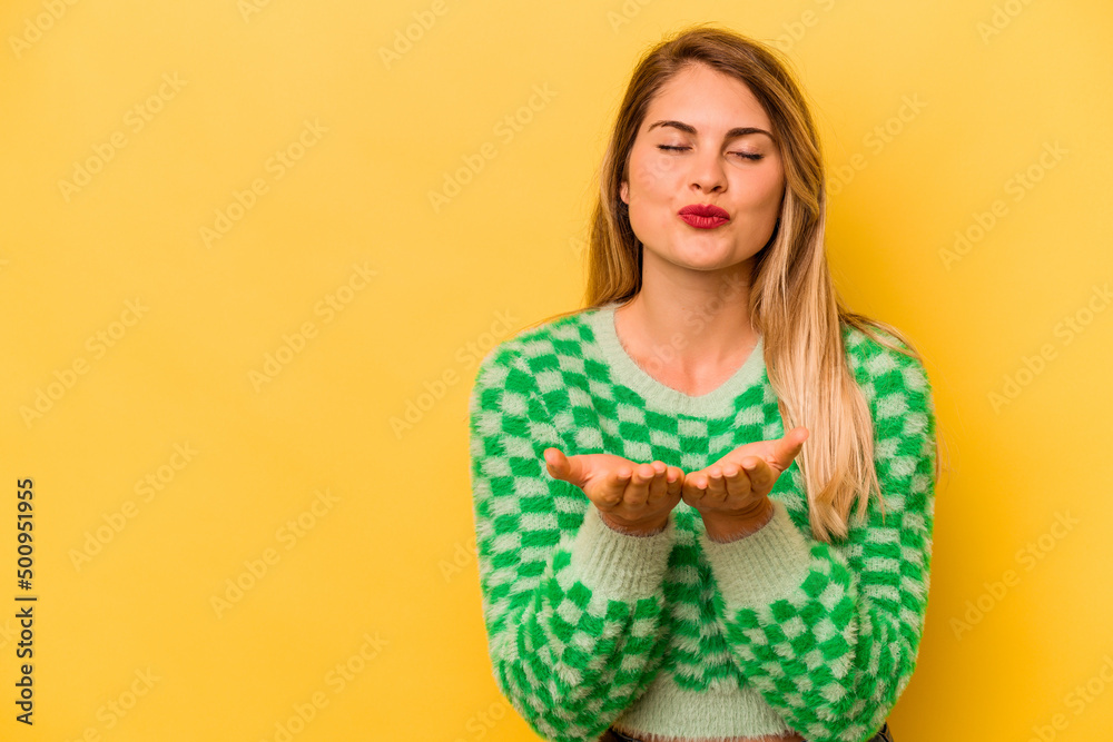 Young caucasian woman isolated on yellow background folding lips and holding palms to send air kiss. Young caucasian woman isolated on yellow background folding lips and holding palms to send air kiss.
