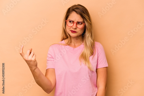 Young caucasian woman isolated on beige background pointing with finger at you as if inviting come closer.