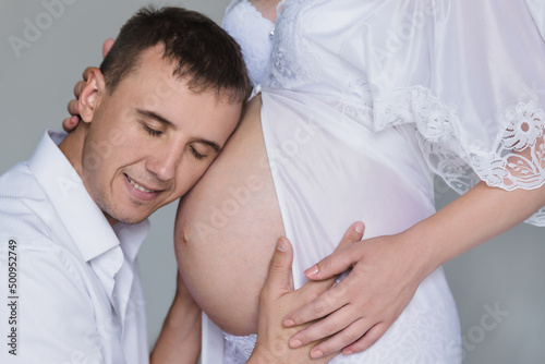 a man listening to his pregnant wife's tummy and smiling, closed eyes closeup