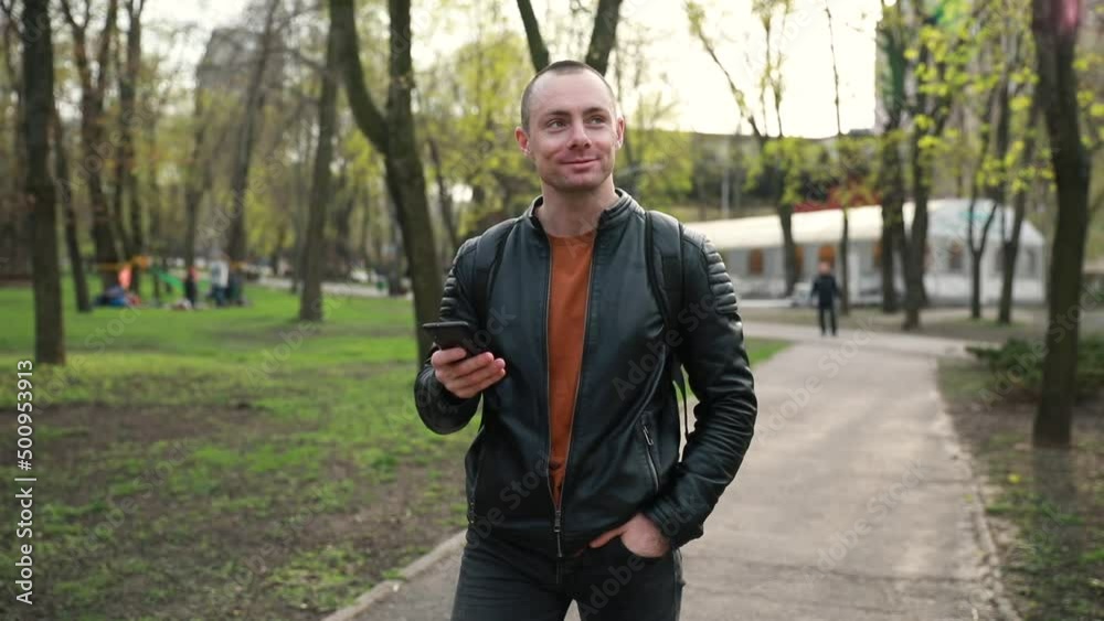 a handsome young cheerful man walks through the park with a phone in his hands. Spring a handsome young cheerful man walks through the park with a phone in his hands. Spring