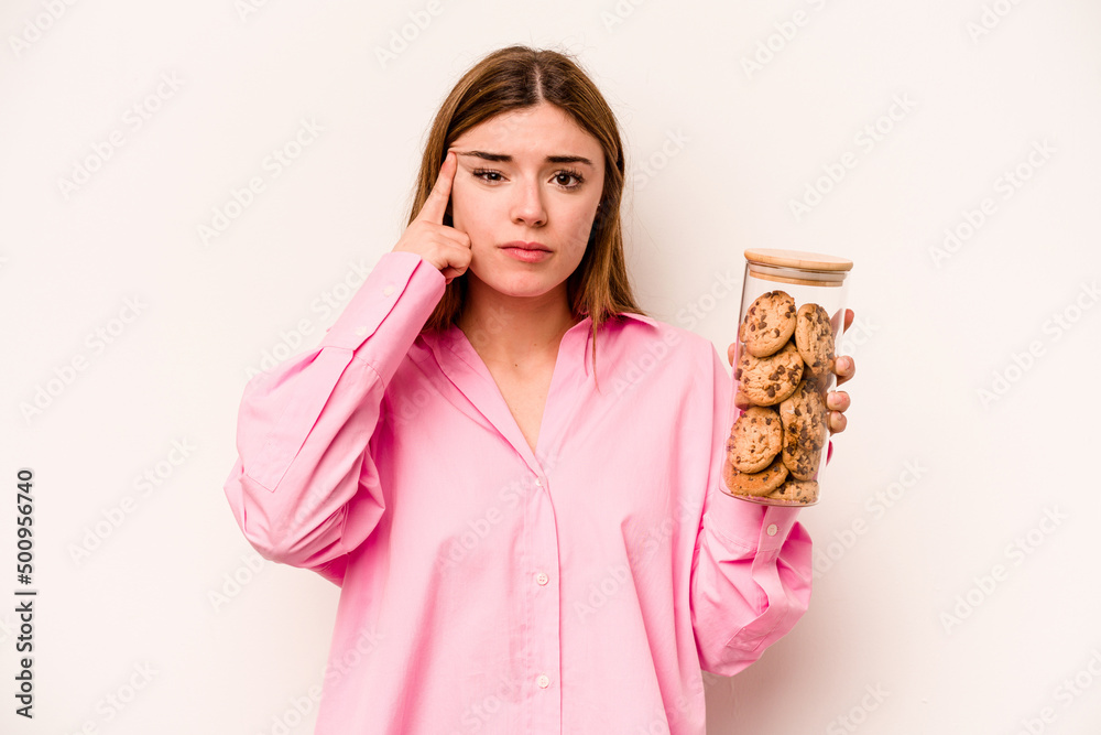 Young caucasian woman holding cookies jar isolated on white background showing a disappointment gesture with forefinger. Young caucasian woman holding cookies jar isolated on white background showing a disappointment gesture with forefinger.