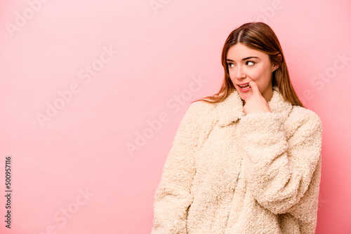 Young caucasian woman isolated on pink background relaxed thinking about something looking at a copy space. © Asier