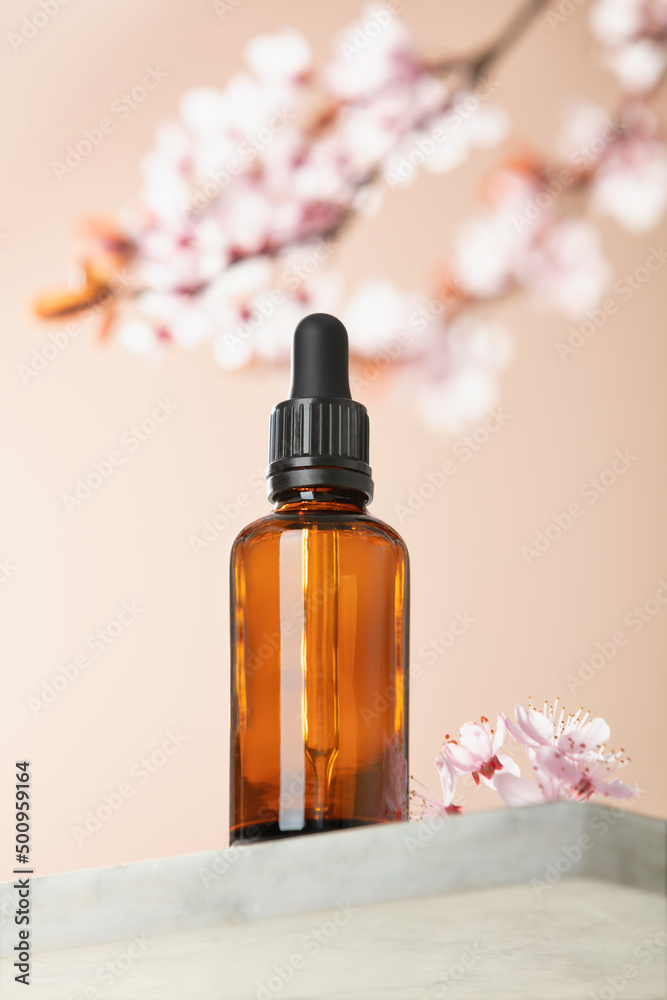 Amber glass dropper bottle and spring cherry blossom flower on marble shelf. Skincare products , natural cosmetic. Beauty concept for face and body care, ow angle view, Amber glass dropper bottle and spring cherry blossom flower on marble shelf. Skincare products , natural cosmetic. Beauty concept for face and body care, ow angle view,