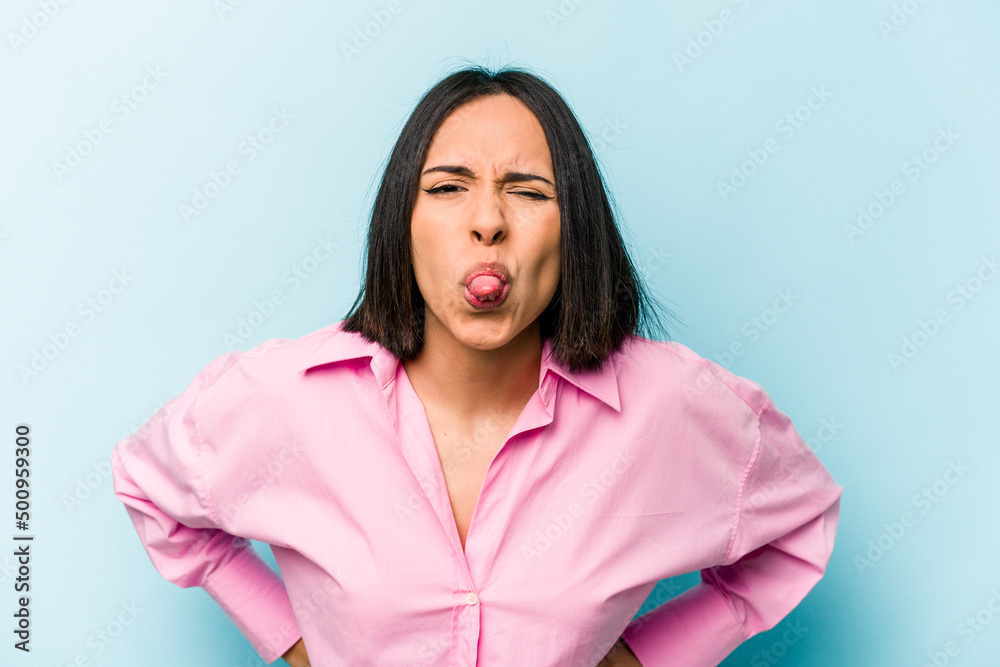 Young hispanic woman isolated on blue background funny and friendly sticking out tongue. Young hispanic woman isolated on blue background funny and friendly sticking out tongue.