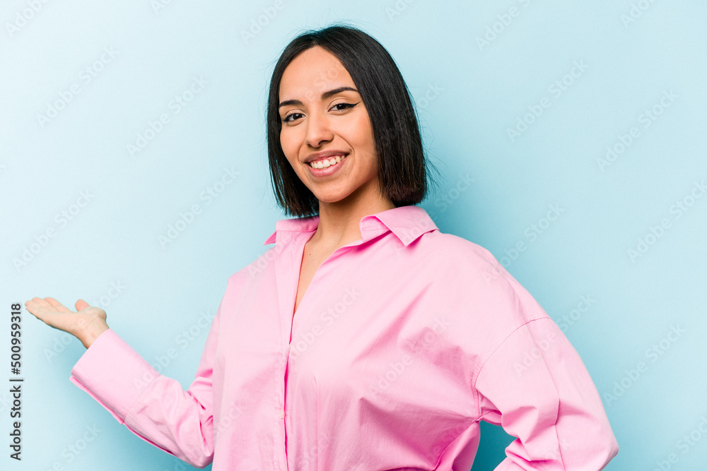 Young hispanic woman isolated on blue background showing a welcome expression. Young hispanic woman isolated on blue background showing a welcome expression.
