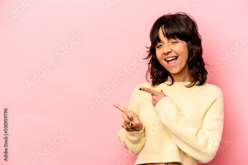 Young hispanic woman isolated on pink background excited pointing with forefingers away.