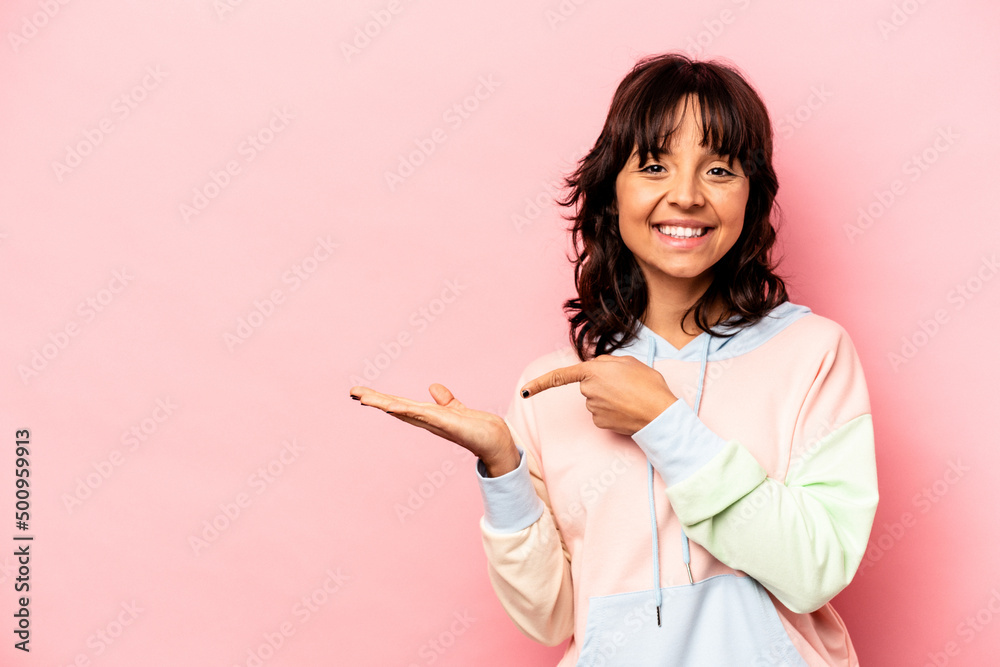 Young hispanic woman isolated on pink background excited holding a copy space on palm.