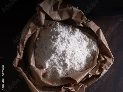 Paper bag, sack, with flour against dark background