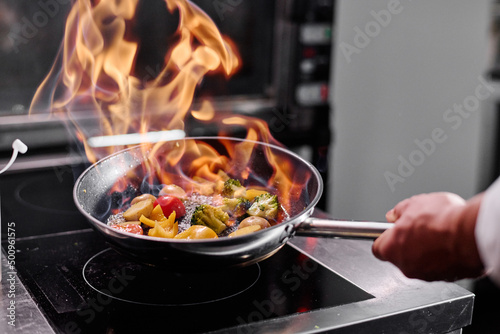 Fototapeta Naklejka Na Ścianę i Meble -  Close-up of professional chef in a commercial kitchen cooking flambe style