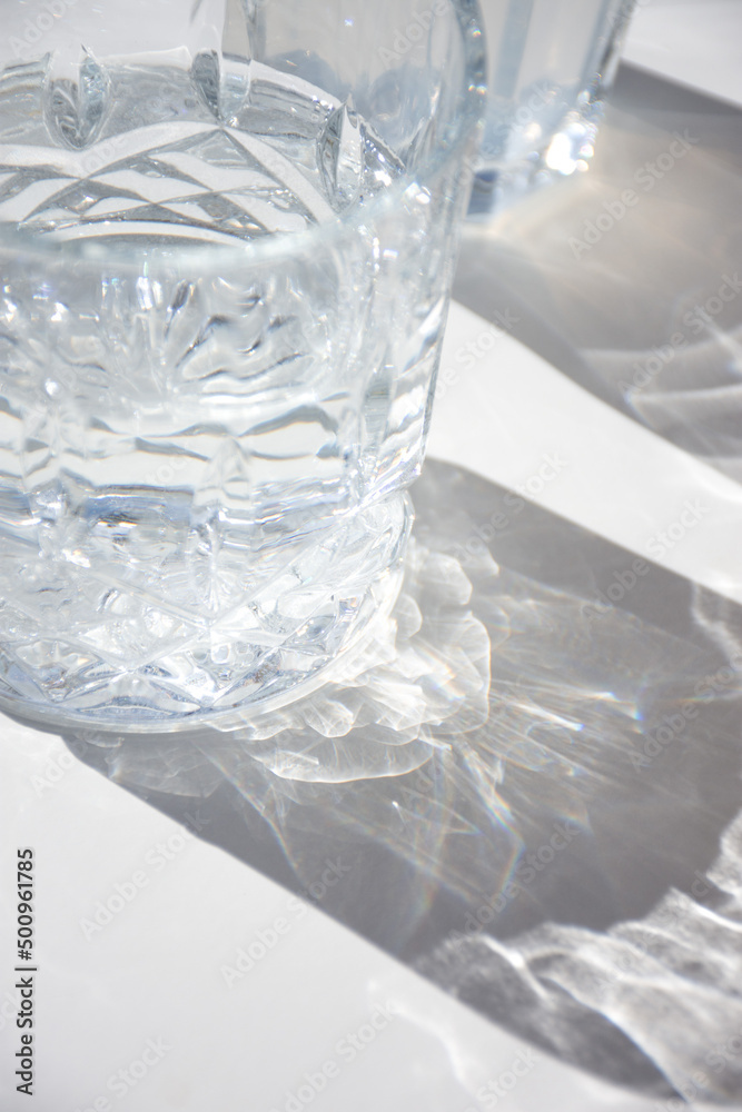 primer plano de un vaso de cristal con agua y su sombra sobre una mesa blanca primer plano de un vaso de cristal con agua y su sombra sobre una mesa blanca