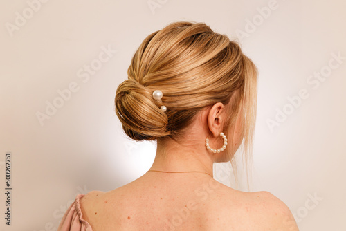 The concept of style, style and beauty. .Photo of a girl from the backside, with a pearl clip in her blonde hair, gathered in a neat bun, on a white studio background. Hairstyle for girls. Close-up