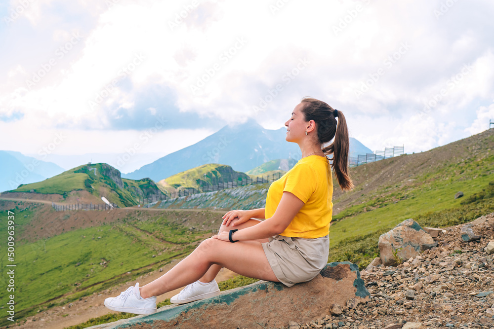 Naklejka premium a girl in a yellow t-shirt sits on a stone and looks at the mountains