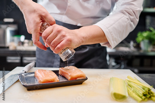 Close-up of chef adding spices on fish meat before cooking japanese dish at table in kitchen