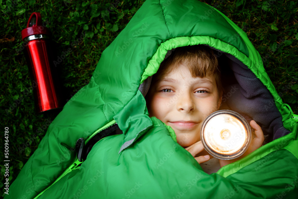 Preteen school kid boy in sleeping bag camping. Outdoors activity with  children in summer. Fun and adventure camp, family and friends vacations or  weekend trip. Portrait of child with flashlight. Photos