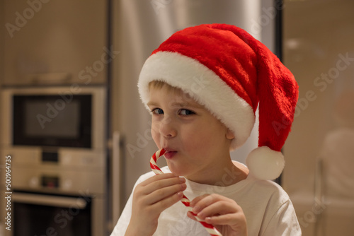 A cute little boy in Santa Claus Christmas red cap eats a striped lollipop. Concept holiday, sweets