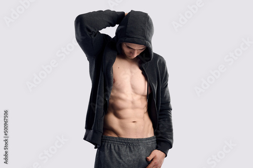 Naked handsome male gym trainer wear hoody with muscular body, strong perfect abs on gray isolated background
