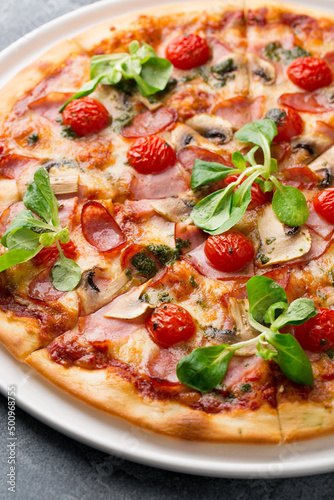Sliced tasty pizza with mushroom, cheese, tomatoes, pepper, becon, sausage, fresh salad and pesto. Italian pizza