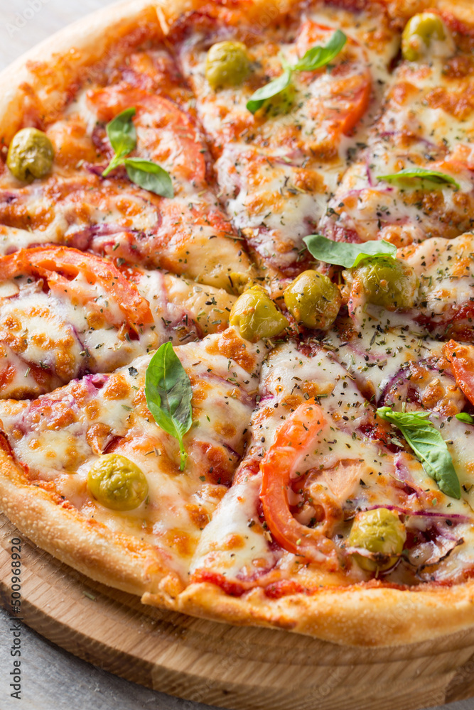 Sliced tasty fresh pizza with cheese, mozarella, olive, onion, tomatoes, spices and basil. Vegeterian italian pizza on wood cutting board Sliced tasty fresh pizza with cheese, mozarella, olive, onion, tomatoes, spices and basil. Vegeterian italian pizza on wood cutting board