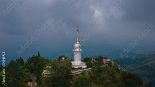 Ambuluwawa tower on top of the mountain where many tourists walk over the spiral stairs  from the view point as the sunlight shifts over the attraction on a cloudy day. Wide drone hyperlapse shot photo