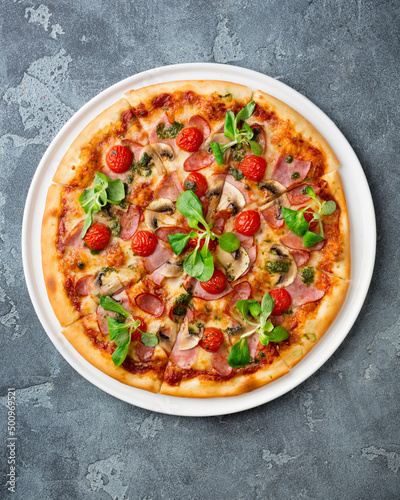 Sliced tasty pizza with mushroom, cheese, tomatoes, pepper, becon, sausage, fresh salad and pesto. Italian pizza, copy space