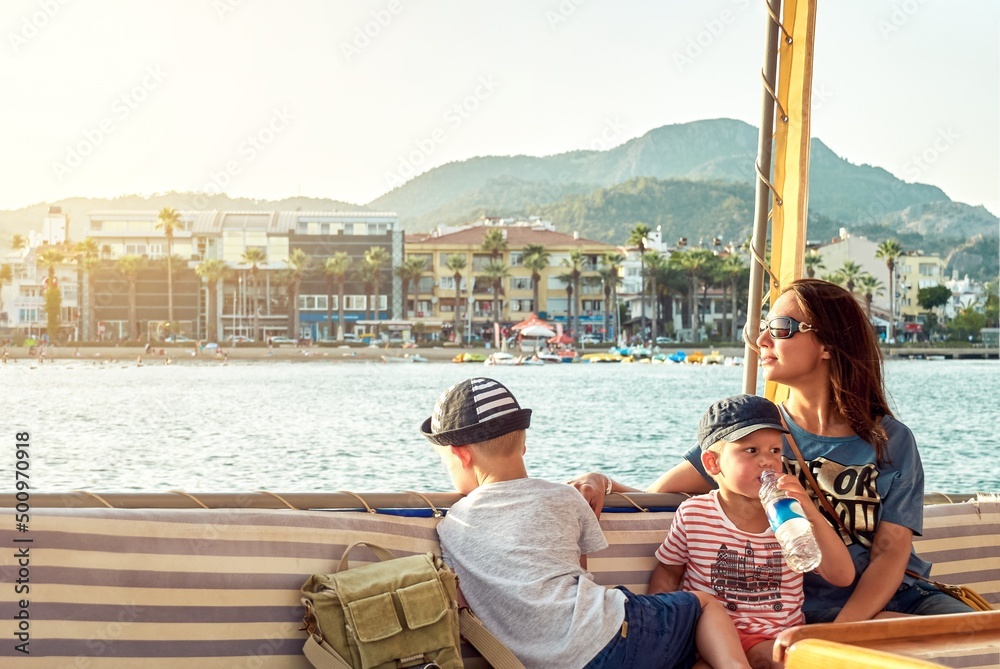Mother and sons relax on boat sailing in sea along coast of Marmaris against mountains. Woman with toddler and preschooler boys enjoy vacation in Turkey