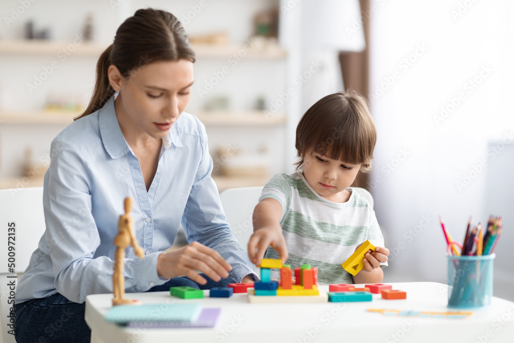 Fototapeta premium Cute little boy preschooler playing developing wooden games with professional woman psychologist at kindergarten
