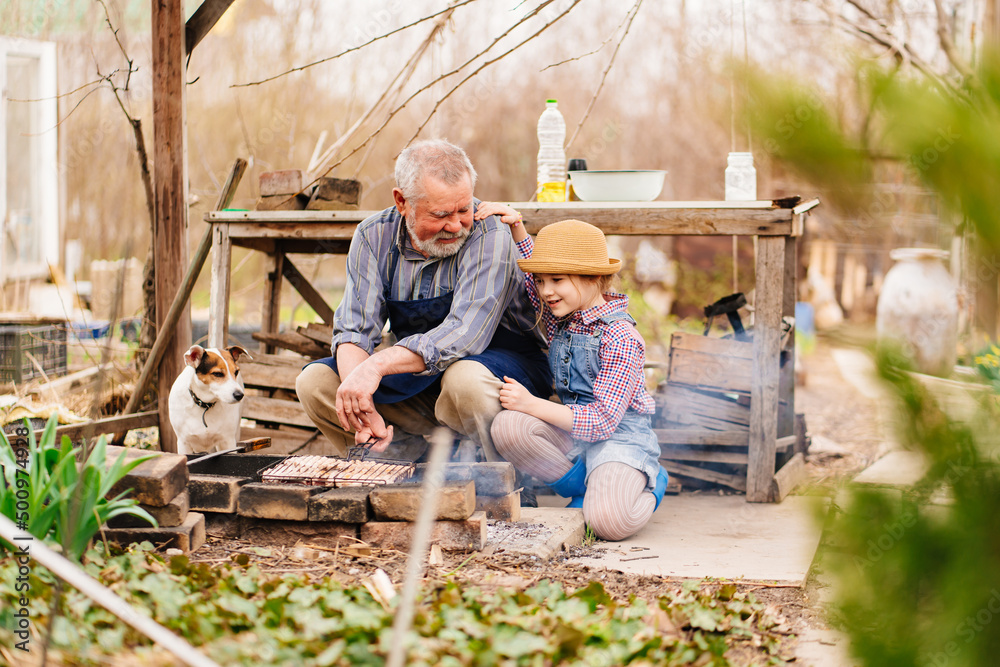 granddaughter helps grandfather with dog cook barbecue on the grill, bonfire granddaughter helps grandfather with dog cook barbecue on the grill, bonfire