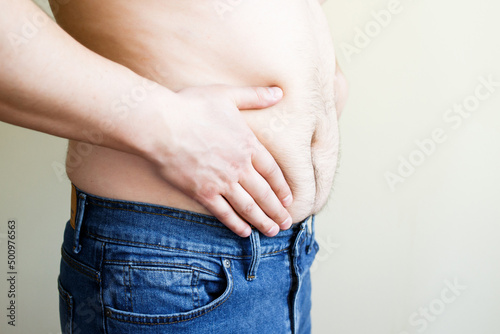 naked belly of a fat man. A man in bad shape. A man in blue jeans on a yellow background. Diet concept. © Iryna Medvedeva