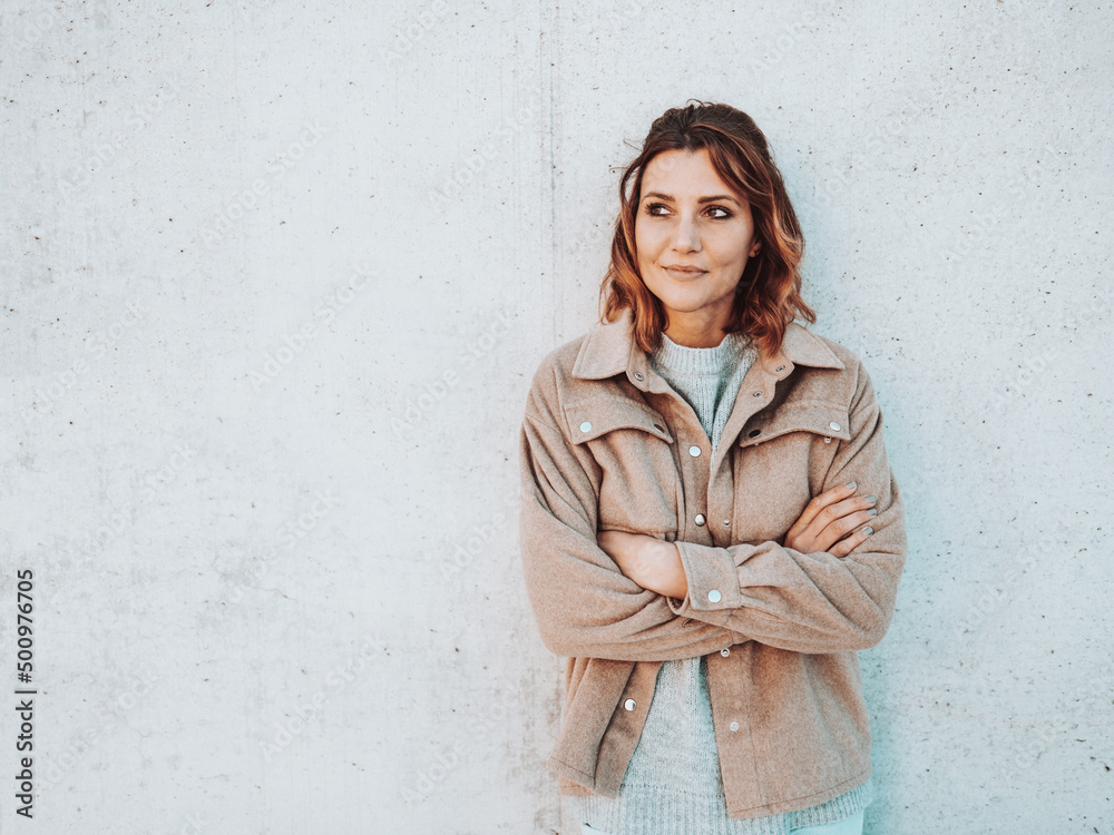 young woman stands laughing with folded arms in front of grey wall young woman stands laughing with folded arms in front of grey wall