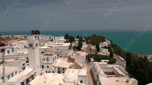 Aerial Backward Shot Of Mosque Amidst Residential Buildings On Hill By Sea During Sunny Day - Djerba, Tunisia