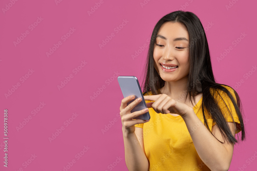 Cheerful asian lady using smartphone for messaging with friends, texting on cellphone, violet background, free space Cheerful asian lady using smartphone for messaging with friends, texting on cellphone, violet background, free space