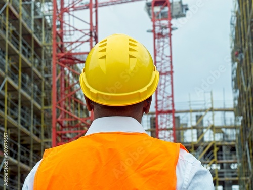 Back turned construction worker with safety jacket and hardhat looking at construction site