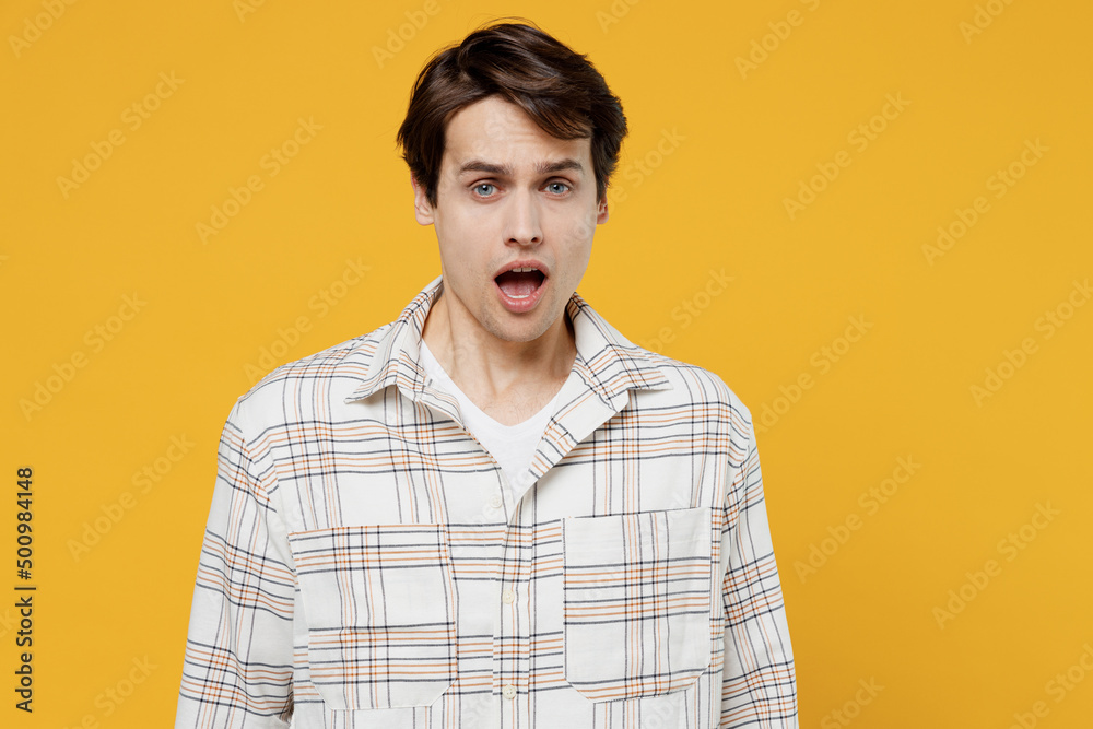 Young shocked surprised sad disappointed happy man 20s wearing white casual shirt look camera with opened mouth isolated on plain yellow background studio portrait. People lifestyle emotions concept.