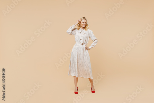 Full size body length blithesome elderly gray-haired blonde woman lady 40s years old wears pink dress hold hand on waist looking down posing isolated on plain pastel beige background studio portrait.