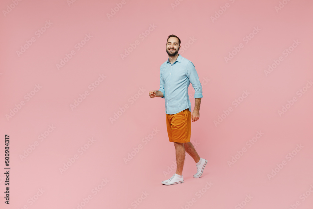 Full body young smiling happy fun cheerful caucasian man 20s wear classic blue shirt walking going look camera isolated on plain pastel light pink background studio portrait. People lifestyle concept.