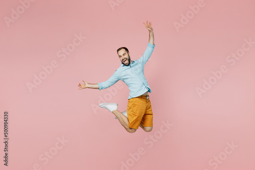 Full size young excited overjoyed winner fun cool happy caucasian man 20s wearing classic blue shirt jump high with outstratched hands isolated on plain pastel light pink background studio portrait
