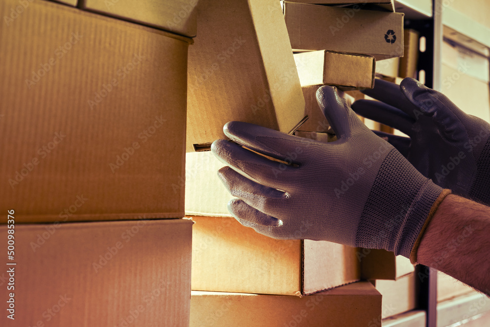 A worker man hands hold cardboard boxes on the shelves of a fully