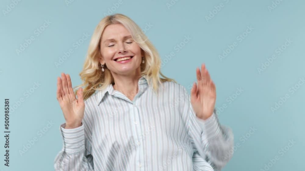 Fun elderly blonde woman lady 40s years old in white shirt dance clench fists waving rising gesticulating hands have fun enjoy celebrate isolated on plain pastel light blue background studio portrait Fun elderly blonde woman lady 40s years old in white shirt dance clench fists waving rising gesticulating hands have fun enjoy celebrate isolated on plain pastel light blue background studio portrait