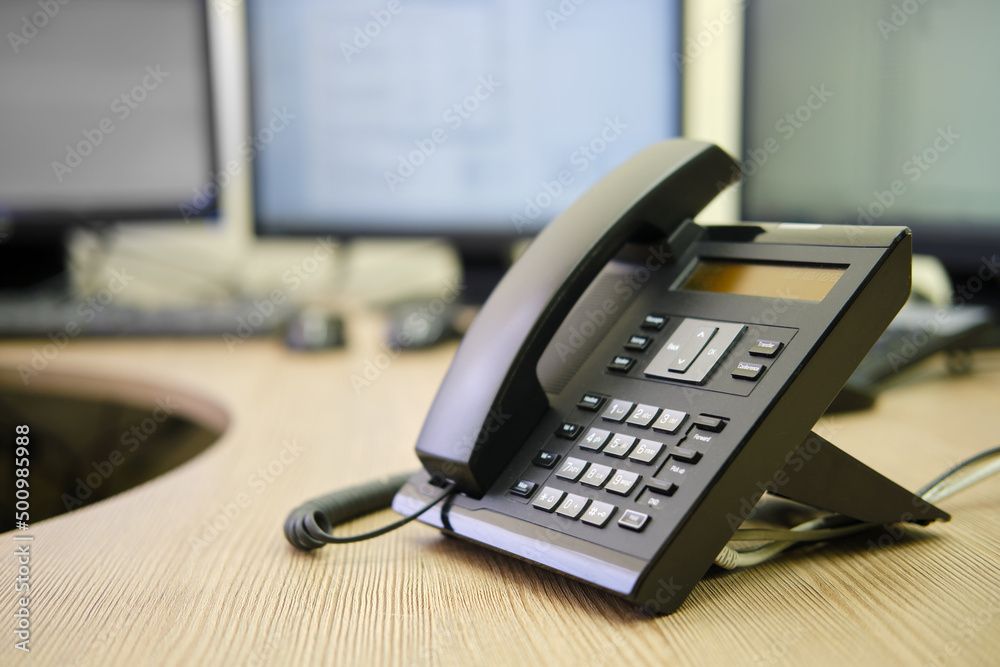 Landline phone on office desk with computer monitors and keyboards Landline phone on office desk with computer monitors and keyboards