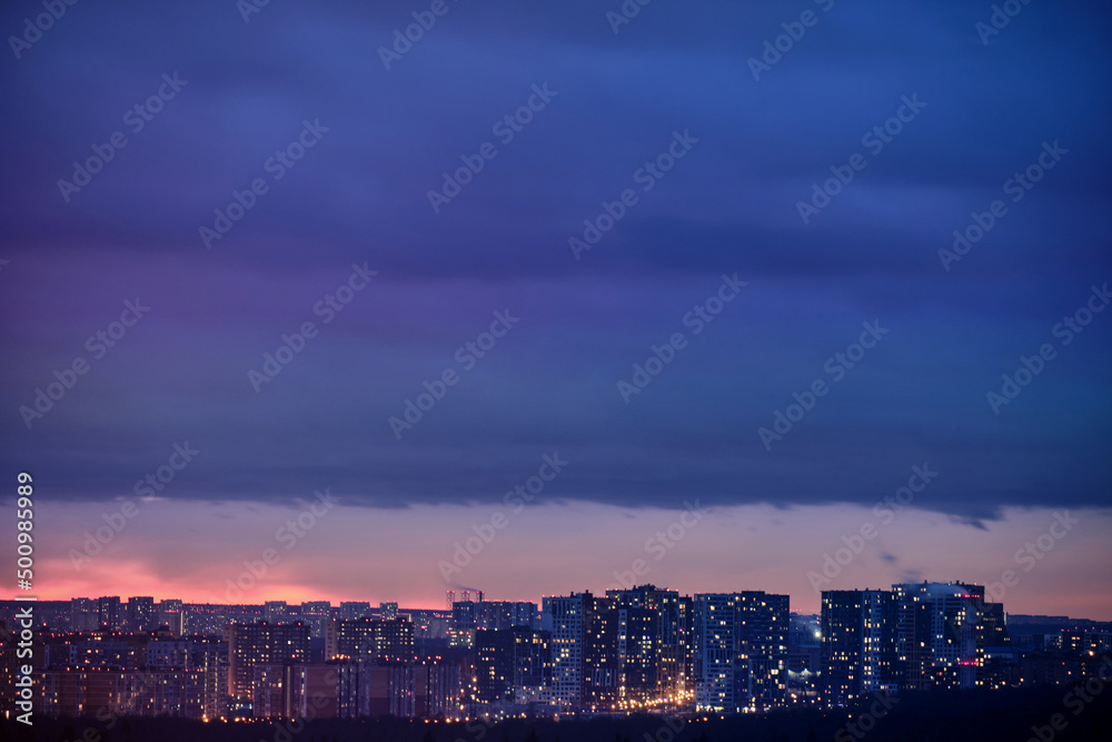 Thunderclouds over a dark city at night with high-rise buildings. Dramatic sky with black clouds over the evening city