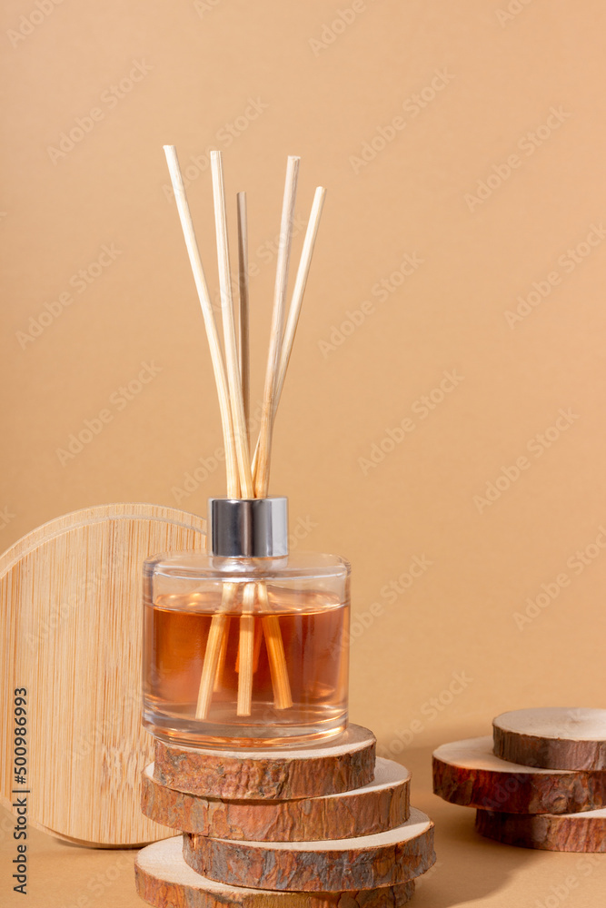 reed diffuser bottle on the podium. Incense sticks for the home with a floral scent with hard shadows. The concept of eco-friendly fragrance for the home - obrazy, fototapety, plakaty 